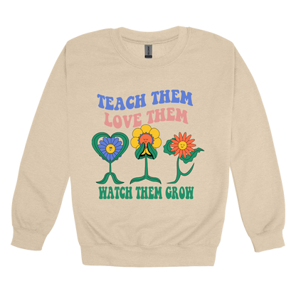 Teach Them Love Them teacher design on Sand adult Crewneck, front view.