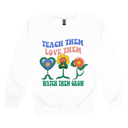 Teach Them Love Them teacher design on White adult Crewneck, front view.